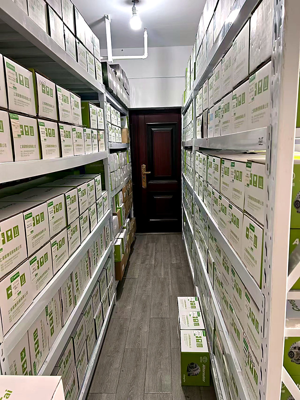Aisle of shelving in the Chengdu warehouse, boxed alternators stacked on both sides and a wooden door at the far end.