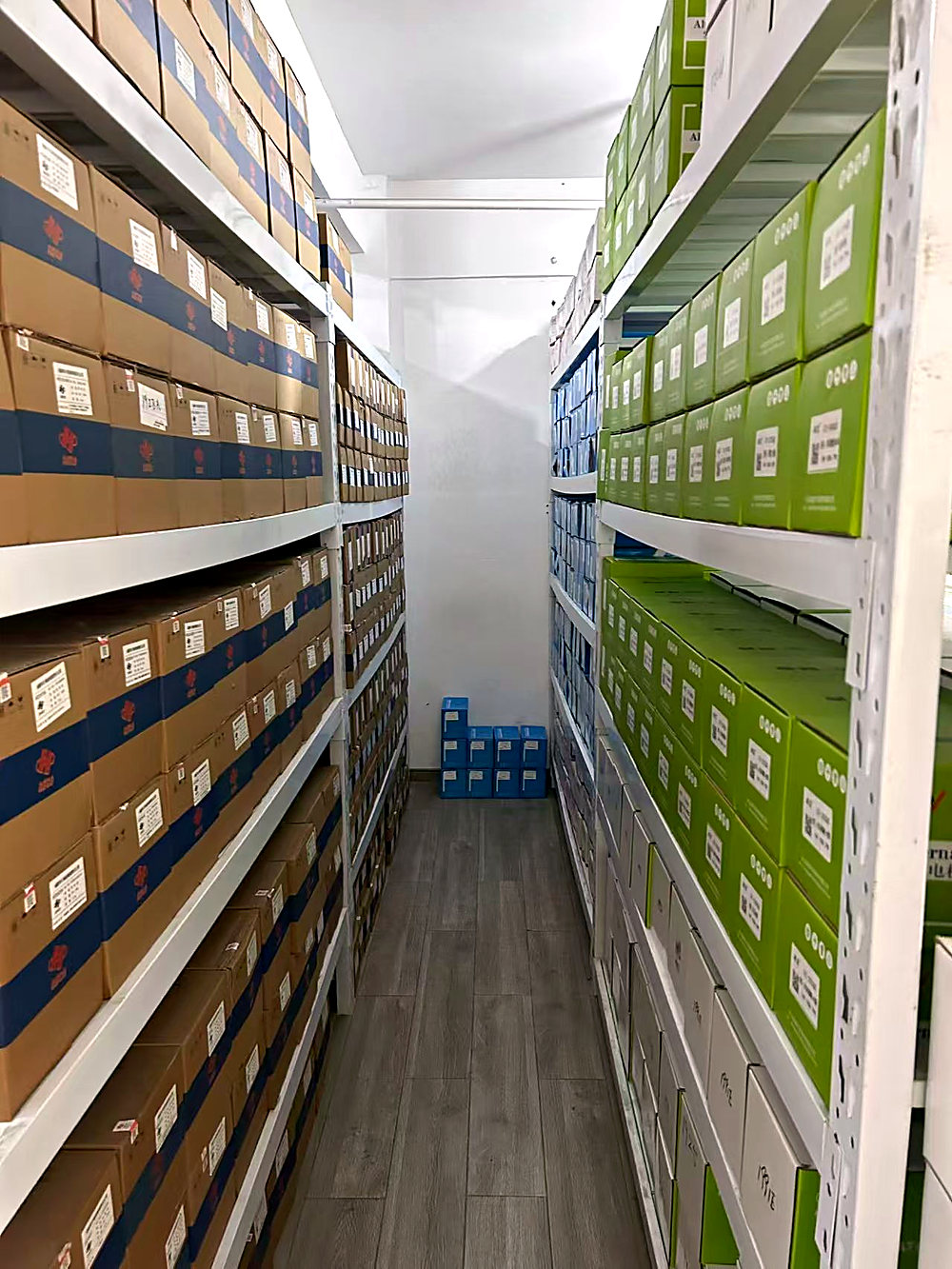 Warehouse aisle with banded brown cartons on the left rack and green cartons on the right.